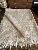 Full view of the folded butter cream mohair blanket showing soft texture and fringe detail.