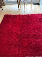 Full view of the cherry red flokati carpet unfolded on a wood floor, showing size and color.