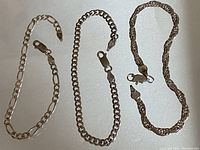 Three sterling silver chain link bracelets laid out flat on white background, showcasing different link styles and lobster claw clasps.
