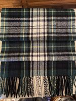 Scarf folded with classic check pattern in black, brown, blue, green, cream, and yellow, with visible fringed ends.