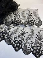 Black lace fabric with scalloped edges laid out flat to show floral and fauna embroidery design.