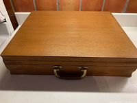 Closed wooden case with brass handle, showing smooth finish and rectangular shape.
