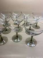 Set of 10 mid-century champagne glasses with smoky grey stems and very light grey bowls arranged in rows.