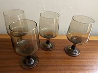Front view of 4 smoky grey wine glasses on wooden surface showing their shape and style