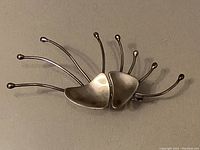 Full view of sterling silver statement pin showing two concave triangular elements with seven spherical-ended posts extending from the edges
