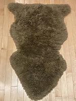 Full view of coffee-colored sheepskin rug laid flat on hardwood floor, showing natural shape and texture.