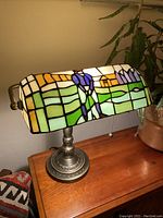 View of the stained glass lamp shade showing a golfer putting, with various shades of green, amber, cream and blue, sitting on a textured metal base with a pull chain.