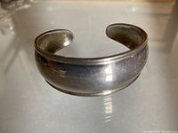 Front and slightly angled view of a sterling silver cuff bracelet showing its polished surface and rolled edges.