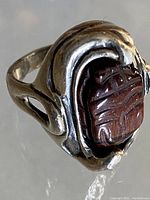 Close-up image of the side profile showing the carved scarab stone within the sterling silver swirling casement. Visible patina on silver and detailed carving on the stone.