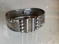 Angled shot of rectangular sterling silver hinged bracelet showing mother of pearl inlay and silver spheres
