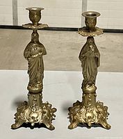 Pair of antique French religious metal altar candlesticks displayed together on white background, showing full height and base design.
