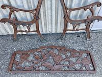 Pair of brown painted wrought iron bench side rails with scroll and leaf design, and a separate matching backrest featuring a large decorative flower and leaves.