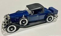 Side profile view of blue and black 1931 Cadillac Roadster diecast model highlighting wheels, body and trunk.
