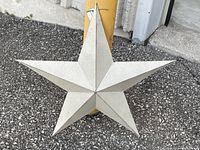 Close-up photo of the metal star on asphalt background, showing its geometric raised facets and light surface finish.