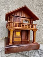 Front view showing two-storey cabin design with balcony, windows, door, and wooden base.
