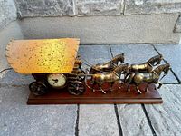 Front view of vintage covered wagon lamp and clock, showing four brass horses, covered wagon with clock, and wood base.