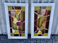Pair of stained glass windows with white painted dovetailed wood frames, featuring fruit and vine designs in amber, yellow, brown, and red.
