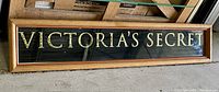 Front view of long horizontal oak framed mirror with ‘VICTORIA’S SECRET’ gold leaf lettering on black mirrored glass