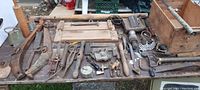 Wide view of table displaying numerous primitive barn items including tools, horse hames, hand tools, locking devices, and wooden press with metal lever