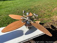 Photo shows the 44-inch ceiling fan assembled with four wooden blades laid out on a table outside. The fan's central metal housing and attached three lights are visible.