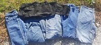 Six pairs of ladies designer jeans laid side by side on grass showing different blue and black denim colors with back pockets visible.