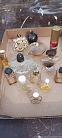 Photo shows a collection of twelve tiny antique perfume bottles in an open cardboard box on a wooden surface, featuring diverse shapes and colorful caps.