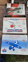 Three die cast airplane models in original boxes including a red and silver plane, a Mobilgas Vintage Airplane Bank, and a blue Amoco airplane bank.
