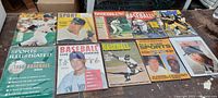 Photo showing a collection of 10 various vintage and modern baseball magazines spread on a wooden table, with players including Mickey Mantle and Cal Ripken on covers.