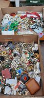 Photo of two large cardboard boxes filled with assorted costume jewelry including necklaces, bracelets, pins and earrings in various colors and materials.