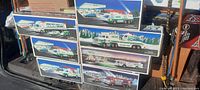 Photo showing 8 Hess toy vehicle sets in their original boxes stacked in two rows, featuring illustrated winter backgrounds and toy trucks with vehicles on the packaging.