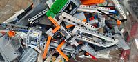 Close-up image of assorted LEGO Technic beams, connectors, and some partially assembled elements in various colors including grey, orange, and green.