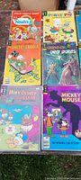 Photo shows a group of eight comics including Walt Disney Mickey Mouse, Huey Dewey and Louie, Grimm's Ghost Stories, Walt Disney's Uncle Scrooge, Noah's Ark, and Porky Pig.