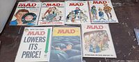 Eight vintage MAD Magazine issues laid out on a surface showing various classic satirical covers