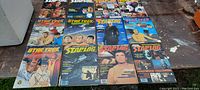 A collection of 17 vintage magazines featuring Star Trek and Starlog, arranged on a wooden surface. Covers prominently show various Star Trek characters and sci-fi themes.