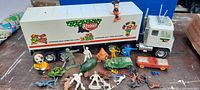 Wide photo showing entire lot of vintage toys with Keebler metal truck, various plastic vehicles, small standing figures and animal figurines on a table.