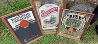Three framed beverage advertising wall signs displayed outdoors on grass, including Windsor Canadian, Dr. McGillicuddy's, and 114 Grand Dad mirror with glass crack.