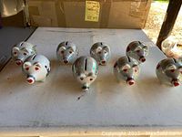 Eight silver porcelain heart piggy banks arranged on a table, showing front and some side views with location/state designs on sides.