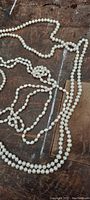 Multiple strands of vintage pearl necklaces displayed on a wooden surface, showing varying lengths and pearl sizes.