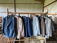 Six men's vintage western-style suit jackets hung on metal rack inside a barn or similar storage area. Jackets show variety of colors and classic Western styling details.
