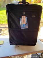 Front view of Samsonite black upright suitcase with attached tags, showing front zippered compartments and retractable handle on top.