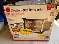 Photo of front of the box showing product name, image of the oven, and selling points like space-saving size and roasting basket.