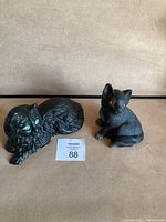 Two black cat figurines: cast iron cat with green eyes on the left, Sandicast cat with amber eyes on the right.