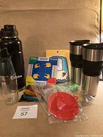 Full view of the lot showing black Bubba water jug, travel mugs, scrubbing pads, trivet, frame, and oil dispenser
