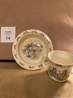 Full view of the Bunnykins ceramic bowl and mug set on a brown surface, showing overall condition and design.