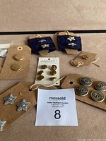 Photo showing multiple sets of buttons and a pair of cufflinks with DT initials on blue fabric.