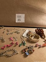Wide view of assorted costume jewellery on brown background including various charm bracelets, plastic animal charms, chains, and pendants.