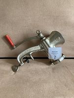 Metal manual meat grinder with large funnel opening and red crank handle laying on surface.