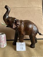 Full side view of brown leather elephant figurine with raised trunk next to soda can for scale.