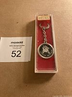 Photo of the metal lunar module keychain in original plastic case with red insert, showing original price tag from NASA Tours.