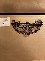 Front view photo of black masquerade mask with intricate metal filigree and red stone accents.